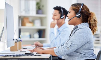 Happy, confident and smiling call centre agent talking on a headset while working on computer in an office. Saleswoman or consultant operating a help desk for customer care and service support