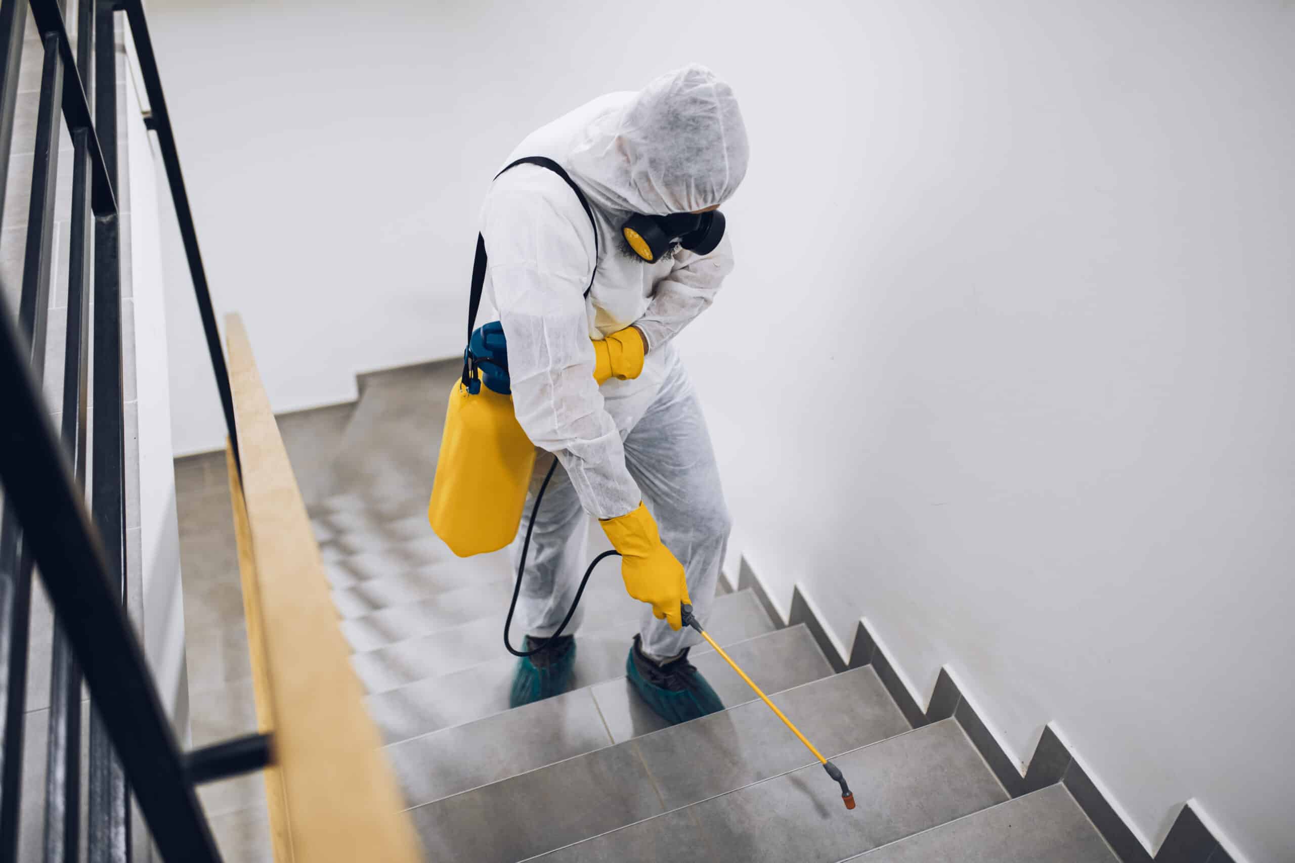 Pest Control exterminator, in work gear spraying pesticide in a stairway.